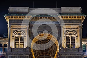 Milan, Italy low angle night shot of illuminated Galleria Vittorio Emanuele II entrance detail with relevant inscription, a 19th-