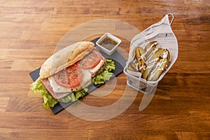 Milanese style sandwich with melted cheese, tomato slices with oregano and ham with lettuce are sauce in a white bowl