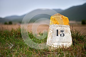 Milestone or milepost sign on a rural road with hills in the bac