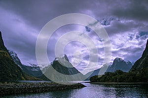 Milford Sound and Mitre Peak, South Island, New Zealand. Steep sided mountains rise from calm waters of the fiord with moody sky