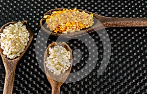 Milho de cor branca e amarela para preparar canjica servida em colheres de madeira sobre um fundo escuro photo