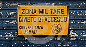 Military area with yellow sign: `Zona militare, divieto di accesso, sorveglianza armata`. Translation: `Milita photo