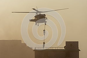 Military combat and war with helicopter flying into the chaos and destruction. Soldiers suspend from rope to the ground from