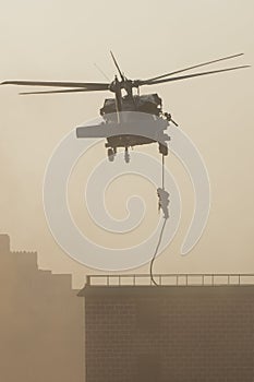 Military combat and war with helicopter flying into the chaos and destruction. Soliders suspend from rope to the ground from