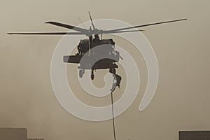 Military combat and war with helicopter flying into the chaos and destruction. Soliders suspend from rope to the ground from