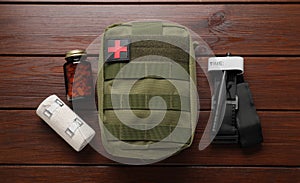 Military first aid kit, tourniquet, pills and elastic bandage on wooden table, flat lay