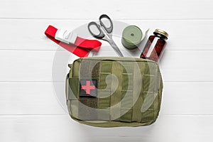 Military first aid kit, tourniquet, scissors. pills and elastic bandage on white wooden table, flat lay