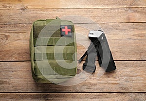 Military first aid kit and tourniquet on wooden table, flat lay