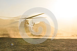 A military helicopter is seen flying and landing in desert at sunset in a cloud of dust. Air force aircraft