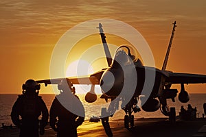 A military jet standing on a sailing navy aircraft carrier during sunset.