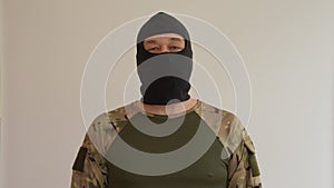 A military man in a black balaclava mask and army uniform on a gray background with a hidden face,