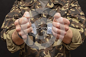 A military man in handcuffs holds an army badge in his hand on a dark background, selective focus. Concept: war criminal, prisoner