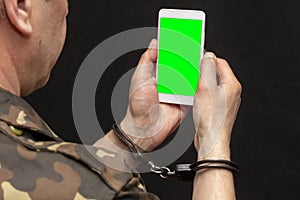 A military man in handcuffs makes a phone call on a dark background, selective focus. Concept: prisoner of war talking on the phon