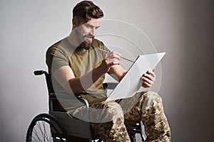 Military man sitting in a wheelchair and painting a picture with a brush