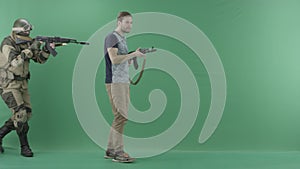 Military man in uniform with machine gun caughts civilian man with a weapon against chromakey background