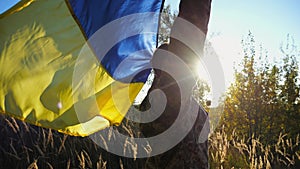 Military man in uniform stands with raised over head flag of Ukraine at countryside. Male ukrainian army soldier with