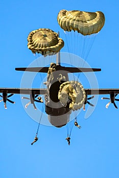 Military parachutist paratroopers parachute jumping out of a air force planes on a clear blue sky day