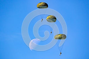 Military parachutist paratroopers parachute jumping out of a air force planes on a clear blue sky day with the moon