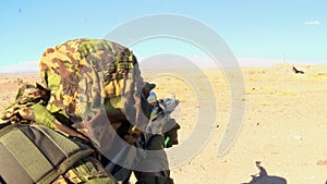 Military soldier aiming a machine gun, lying on the sand in ambush
