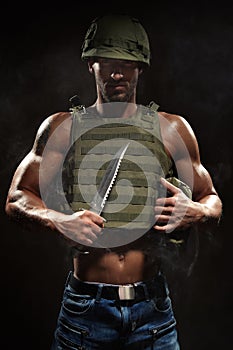 Military style muscle man in tactical vest and helmet posing with survival knife