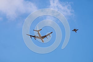 Military tanker aircraft refueler and fighter jet fly on blue sky background