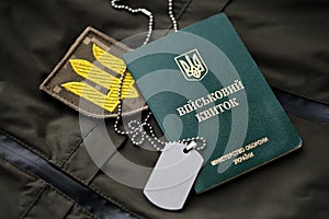 Military token or army ID ticket lies on green ukrainian military uniform