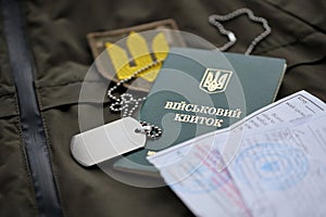 Military token or army ID ticket with mobilization notice lies on green ukrainian military uniform