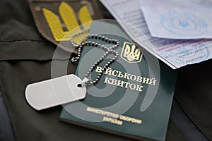 Military token or army ID ticket with mobilization notice lies on green ukrainian military uniform