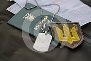 Military token or army ID ticket with mobilization notice lies on green ukrainian military uniform