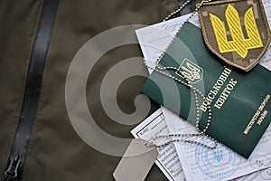 Military token or army ID ticket with mobilization notice lies on green ukrainian military uniform