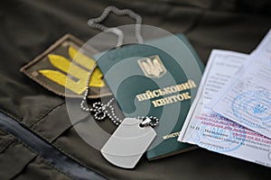 Military token or army ID ticket with mobilization notice lies on green ukrainian military uniform