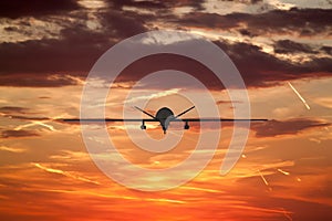 military UAV airplane flies against backdrop of beautiful sunset sky is orange with clouds and condensation traces