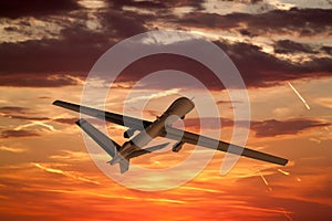 military UAV airplane flies against backdrop of beautiful sunset sky is orange with clouds and condensation traces