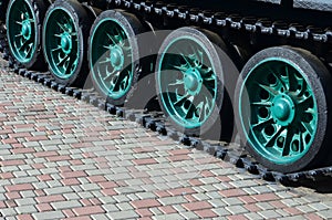 A military vehicle on caterpillar tracks stands on a square of paving stones. Photo of green caterpillars with metal wheels that