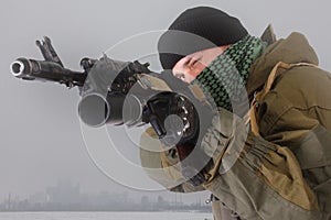 Militiaman in russian pattern uniform with kalashnikov ak-47 rifle with under-barrel grenade launcher at snow field near abandoned