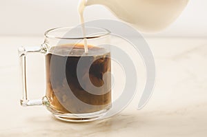 Milk is added to coffee glass/milk is added to coffee glass on white marble background. Selective focus
