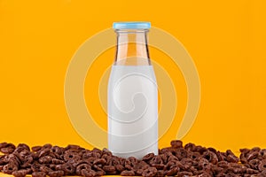 Milk bottle and chocolate cereals on yellow background