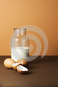 Milk in a bottle with eggs shells on brown background