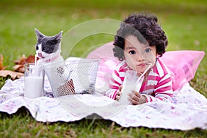 This milk is the cats pajamas. an adorable little girl drinking milk on the grass next to her kitten.