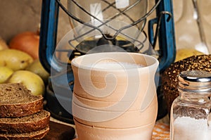 Milk in ceramic ware, rye bread, salt shaker with salt, vegetables and kerosene lantern on a wooden table