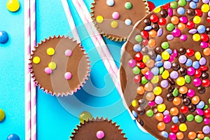 Milk chocolate birthday cake with multicolored glazed candy sprinkles decoration peanut butter cups on blue background. Kids party