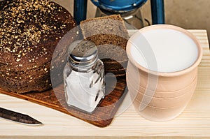 Milk in a clay pot, bread, salt on a cutting board