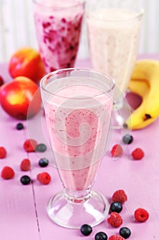 Milk cocktail with banana, blackcurrant and raspberry in a glass on purple wooden background