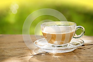 milk coffee in a coffee cup on a vintage old dark wooden table texture and blurred green leaf background