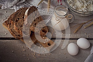 Milk, cottage cheese, sour cream, multigrain homemade bread, fresh eggs and wheat on rustic wooden background.