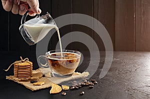 Milk cream poured into coffee cup, latte, cappuccino on wooden table black background and dark colors