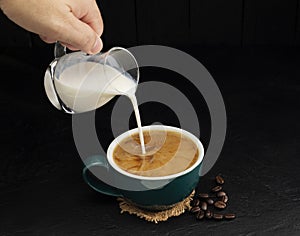 Milk cream poured into a green coffee cup on a wooden table, black and dark background