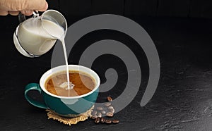 Milk cream poured into a green coffee cup on a wooden table, black and dark background