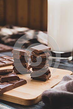 Milk dark chocolate tiles on wood cutting board, wooden background