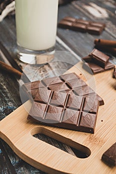 Milk dark chocolate tiles on wood cutting board, wooden background